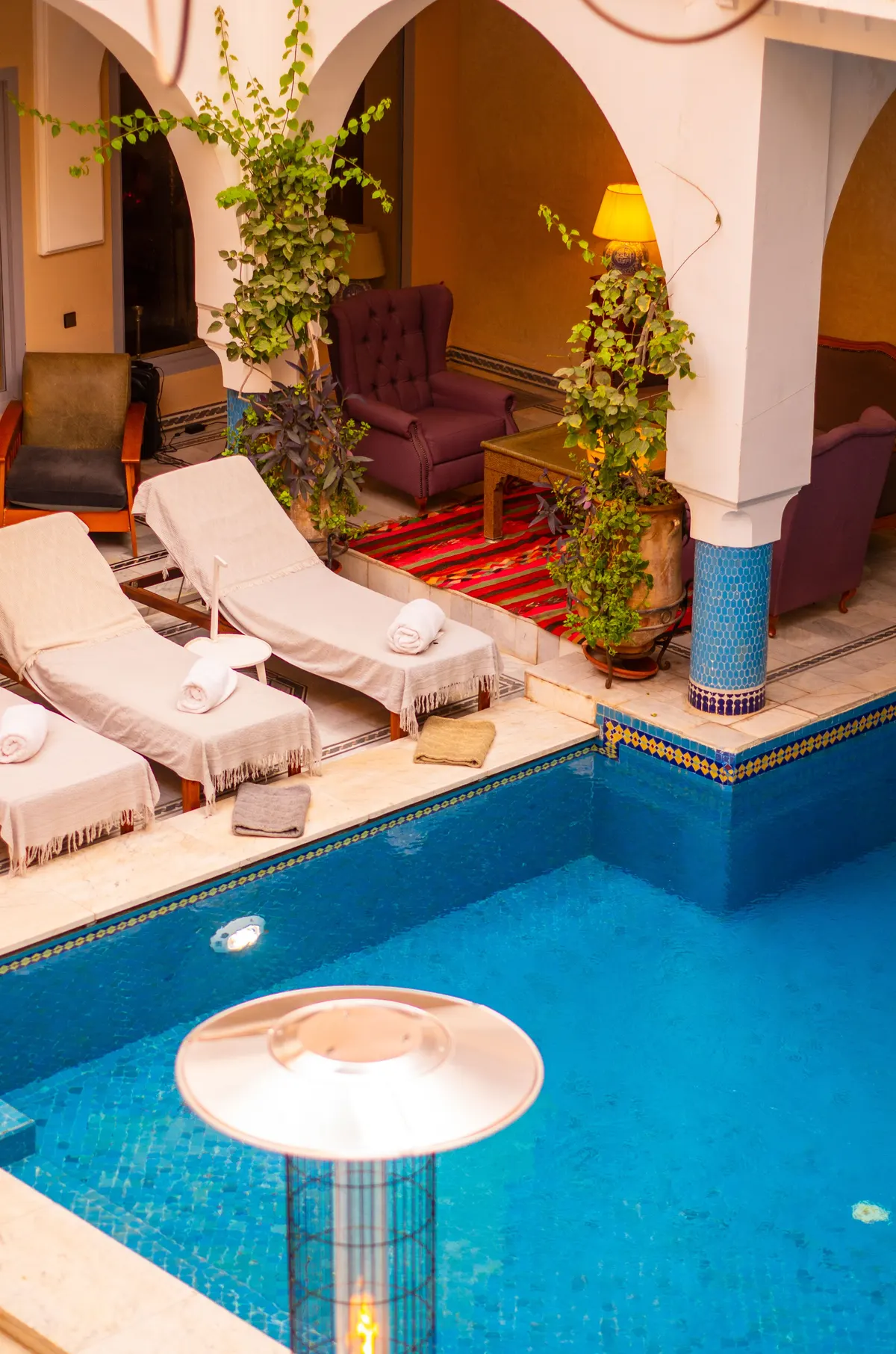 Riad courtyard in Marrakech at dusk: turquoise plunge pool, linen loungers and lantern-lit archways